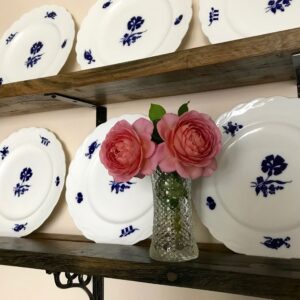 A still life with roses in a glass vase in front of blue and white plates