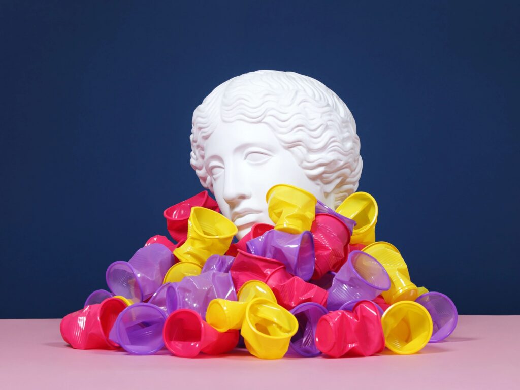 Plaster head buried in disposable plastic cups. Pollution concept