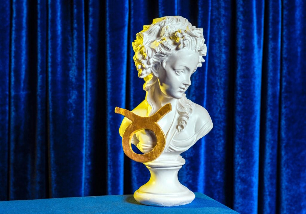 A female plaster bust with the golden sign of Taurus on the background of blue velvet curtains still life.