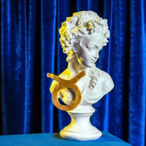 A female plaster bust with the golden sign of Taurus on the background of blue velvet curtains still life.