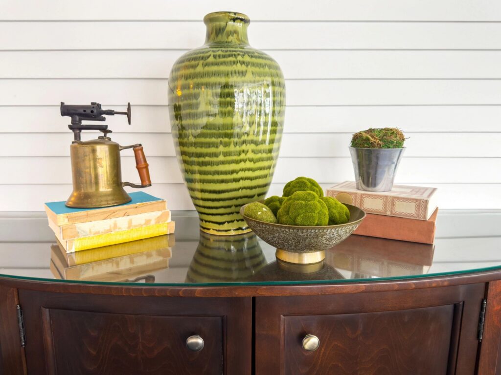 Styled home decor vignette with green ceramic vase and vintage brass objects on wooden sideboard