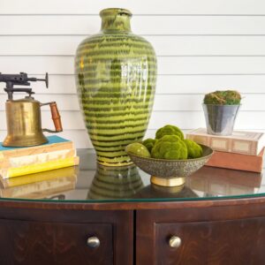 Styled home decor vignette with green ceramic vase and vintage brass objects on wooden sideboard