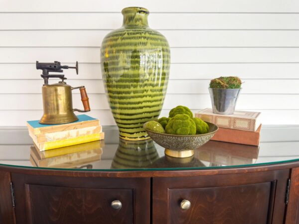 Styled home decor vignette with green ceramic vase and vintage brass objects on wooden sideboard
